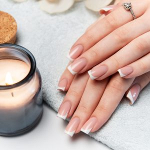Woman's hands with perfect french manicure resting on soft towel next to burning candle and orchid flower, creating relaxing spa atmosphere